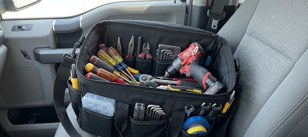 Technician's tool bag open on a truck seat, with screwdrivers, pliers, hex keys and a cordless drill